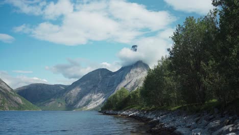 Green-Trees-Along-The-Shoreline-Of-Lake-With-Stetind-Mountain-Peak-In-The-Background-In-Norway