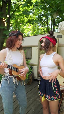 two girls playing ukulele by a camper van