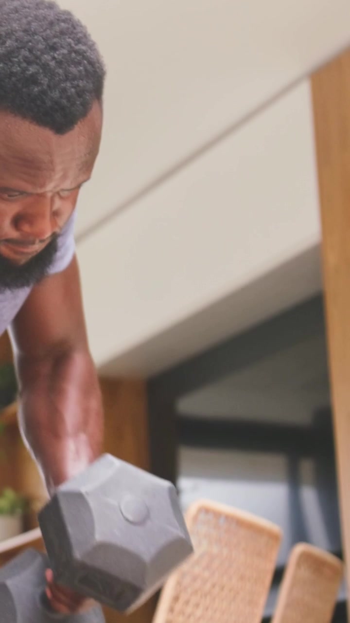 Vertical video: Bracing on bench, man pulling hex dumbbell in common area, gray tee, white watch