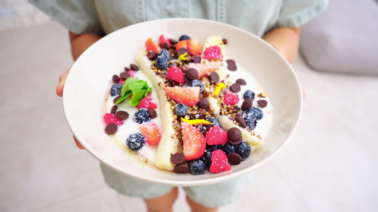 Girl Holding A Plate Of Healthy Banana Split With Mixed Berries, Chocolate Chips And Yogurt. - closeup shot