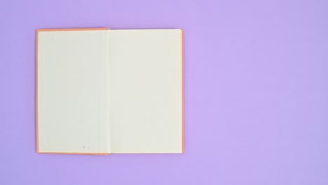 orange hardcover vintage book appear on purple theme and open. stop motion flat lay