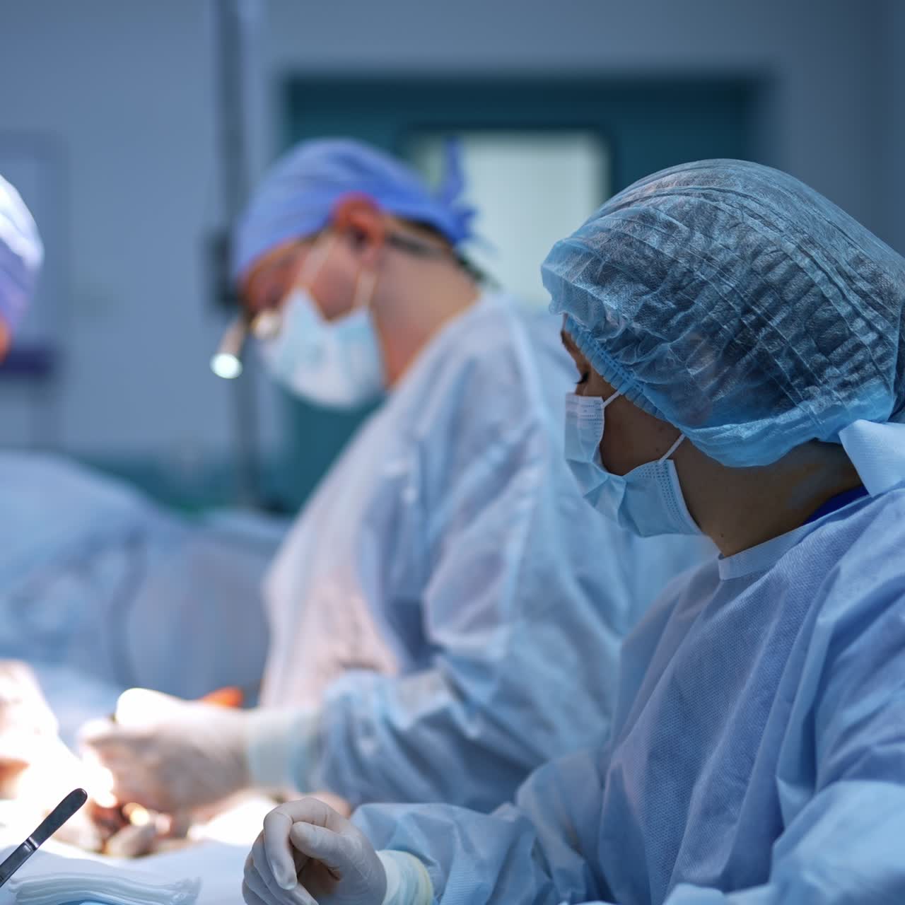 Nurse passes the syringe to the doctor at operation. Chief surgeon with device glasses on head uses electric appliance. Blurred backdrop