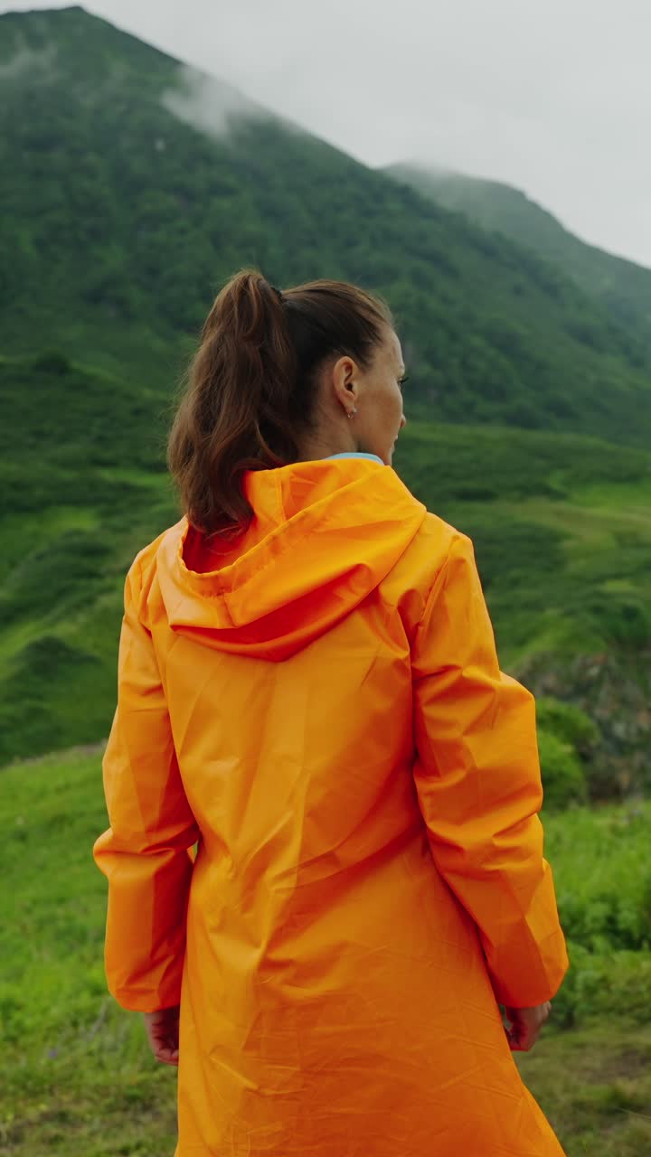 Woman in Orange Raincoat Looking at Green Mountain Landscape