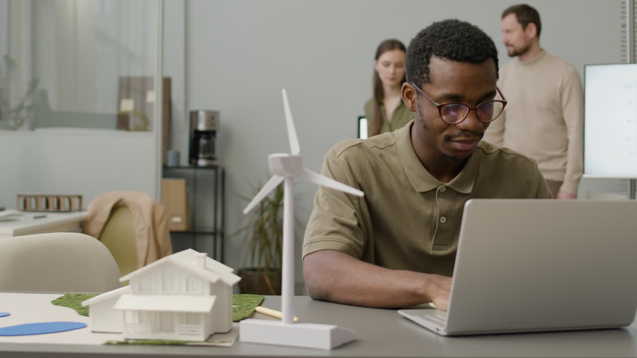 Businessman Using Laptop Sitting At Table With Windmill Model In The Office 3