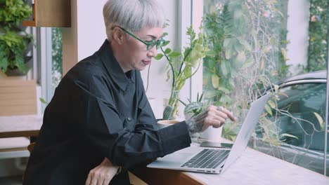 Asian senior woman working on laptop computer on desk in the coffee shop, elderly businesswoman or freelance using notebook to internet online for relax, startup business and communication concept.