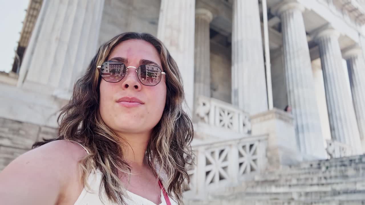 Donna che fa vlogging del suo viaggio ad Atene presso la facciata di un edificio universitario