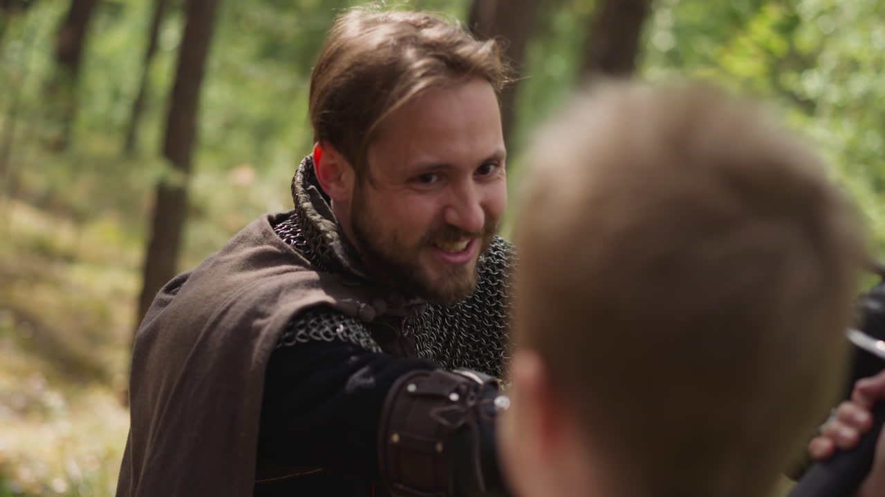 기사 갑옷을 입은 남자가 캠프에서 검을 쓴 소년과 싸운다.