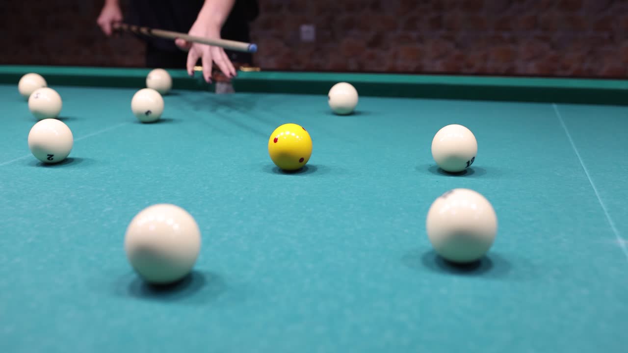A person playing billiards, aiming to hit the yellow ball with a cue