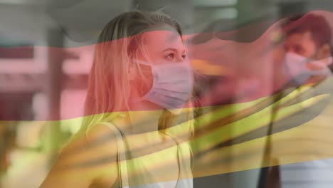 Animation-of-flag-of-germany-waving-over-diverse-woman-and-man-wearing-face-mask-in-city-street