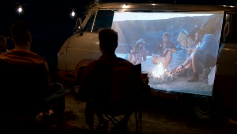 friends watching movie in campsite