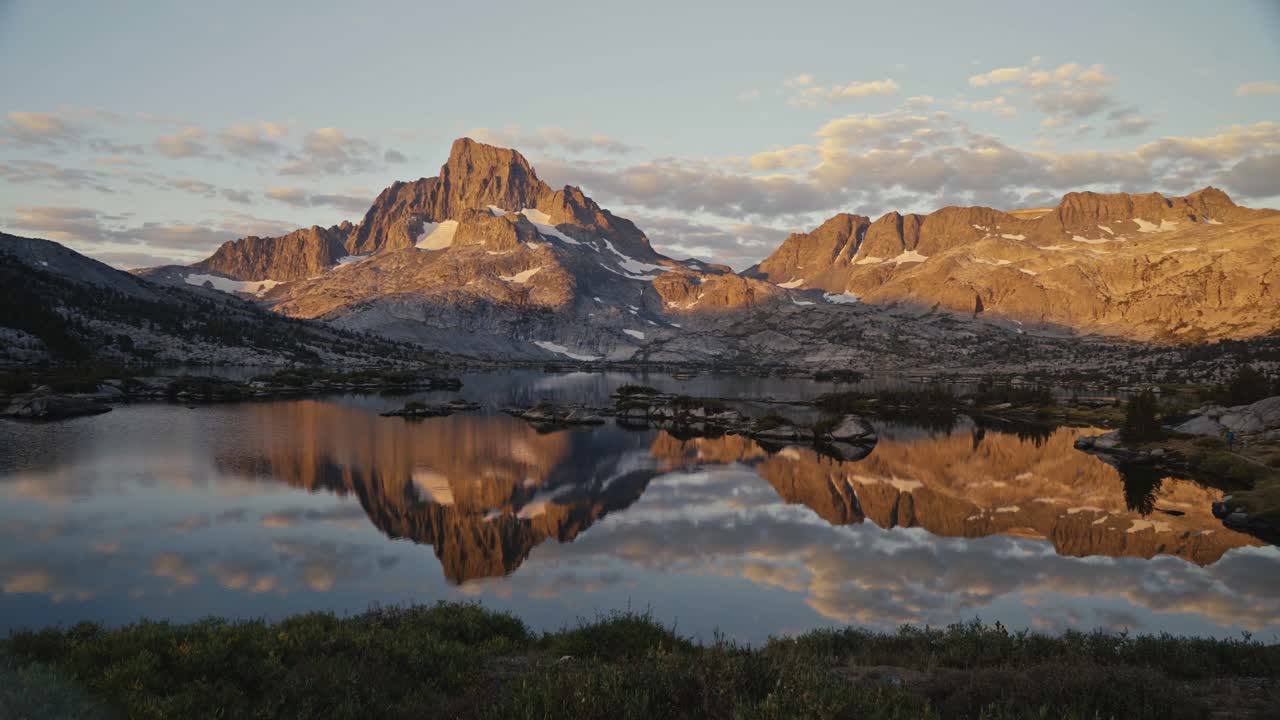 Golden hour reflection of mountains on a calm lake along the John Muir Trail with scattered clouds