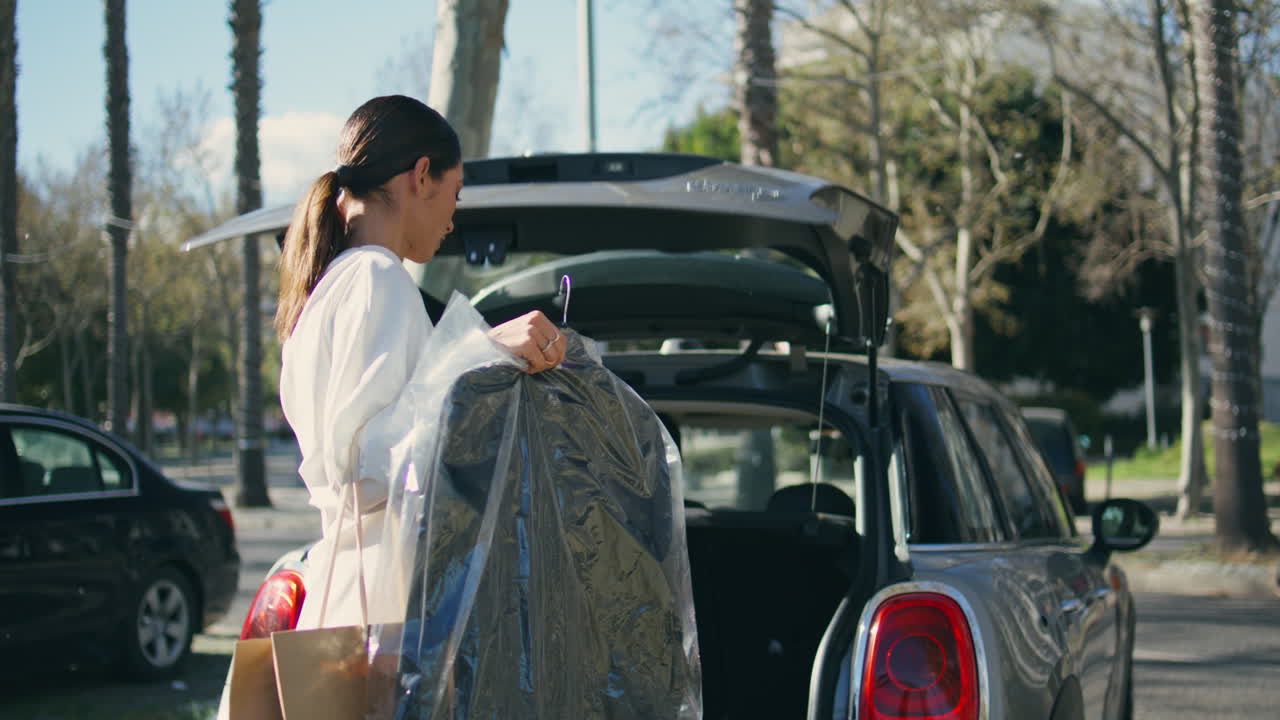 Woman putting clothes trunk automobile sunny day. Lady hiding suit inside car.