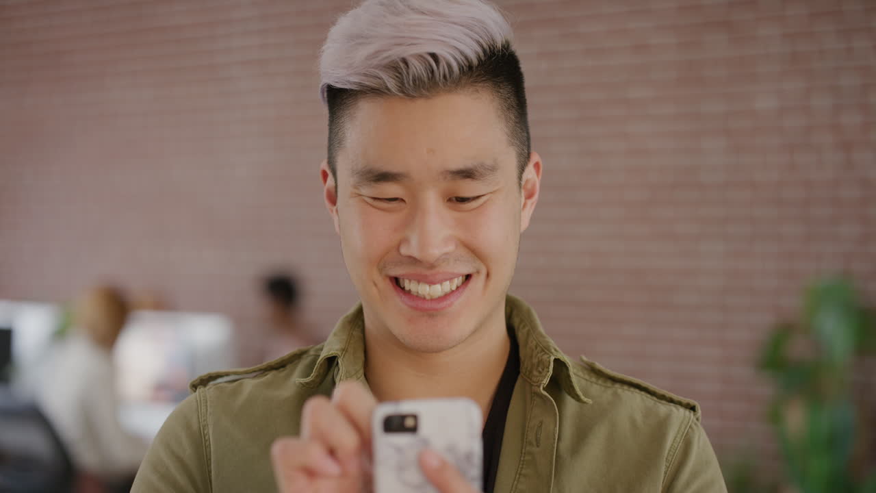 초상화 스타일리시한 젊은 아시아 남자가 스마트폰을 사용하여 문자 메시지를 보내고 휴대폰 앱에서 온라인 메시지를 검색하고 디지털 커뮤니케이션을 즐기며 미소 짓고 만족합니다.