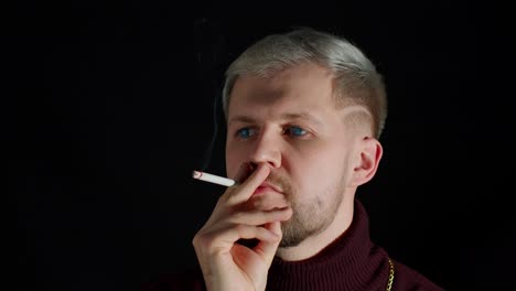 Un-Joven-Adicto-Con-Estilo-Con-Ojos-Azules-Y-Ropa-De-Moda-Mirando-La-Cámara,-Fumando-Cigarrillos