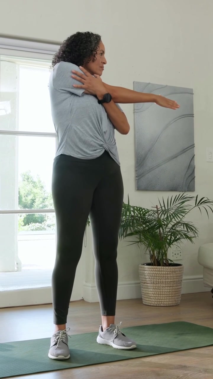Video verticale: Donna in maglietta che dà un'occhiata alla porta e fa stretching per le spalle per l'allenamento su un tappetino verde.