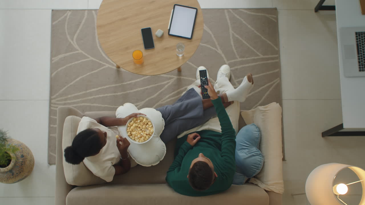 Diverse Relaxed Couple on Couch Watching TV and Eating Popcorn
