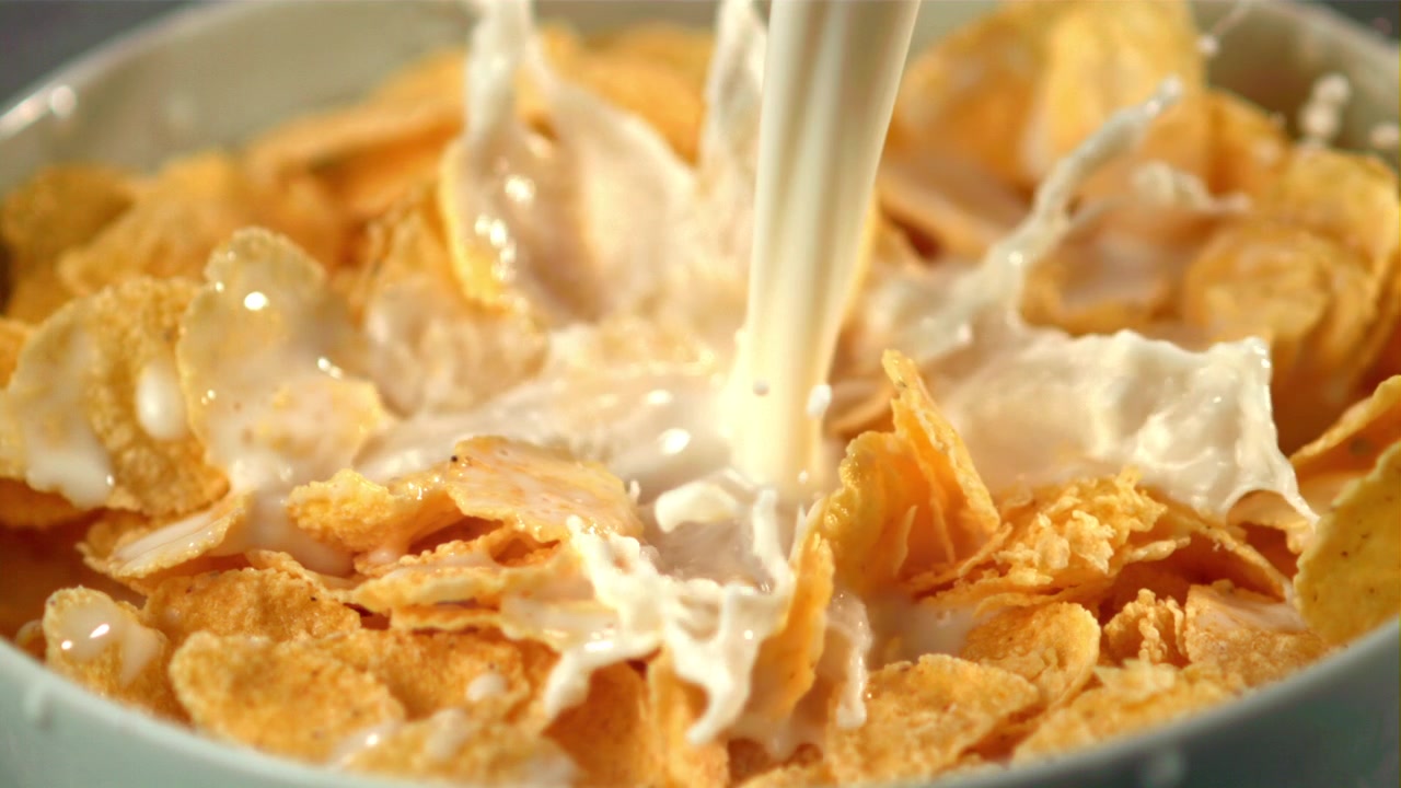 Milch gießt in Zeitlupe auf goldene Cornflakes in einer Schüssel.