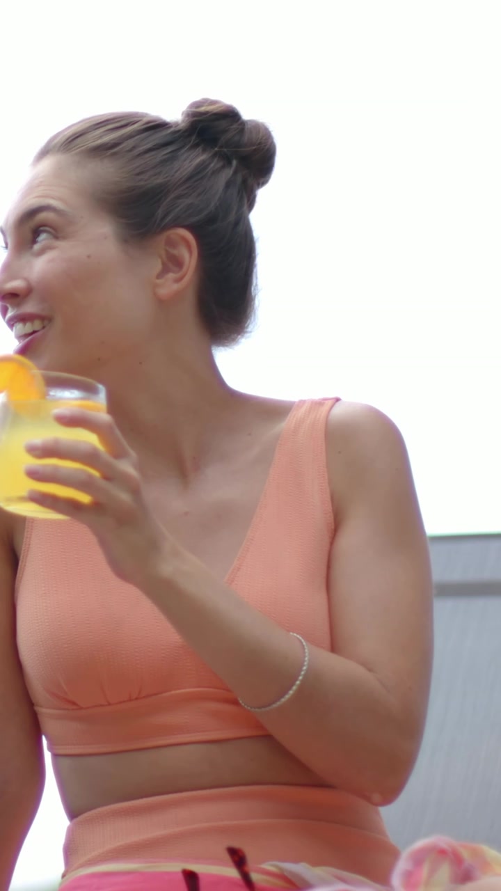 Donna adulta che reagisce a una chiamata fuori campo su una terrazza, tenendo in mano una bevanda all'arancia, rivelando una sdraio da viaggio.