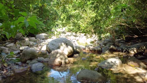 Scenic-View-Flying-Through-Forest-Over-Rocky-Boulders-With-Low-Flowing-River-In-Santa-Marta,-Colombia