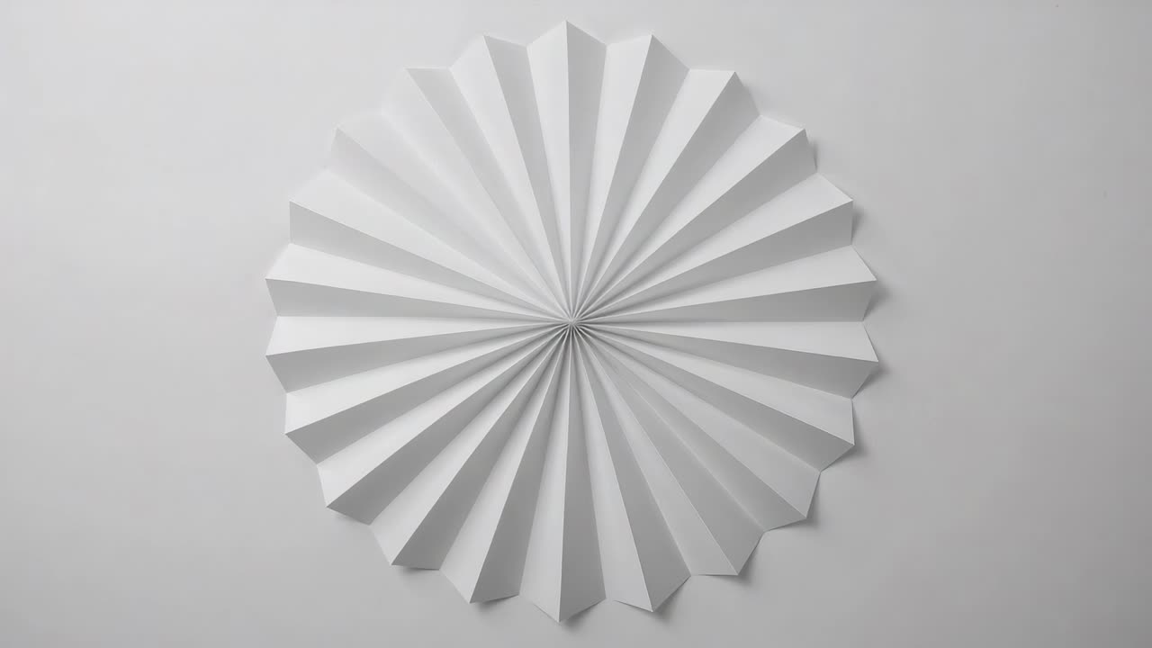 Rotating white pleated rosette turning from pivot on light-gray wall, revealing shifting shadows