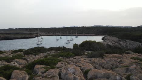 Drone-view-of-coral-cliffs-and-boats-at-Cala-Varques-beach,-Mallorca,-Spain