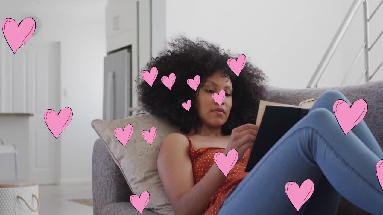 Animation of social media heart icons over biracial woman reading book on sofa