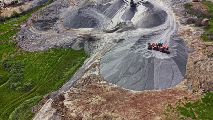 Granite quarry operation shows heavy machinery and stone piles during a sunny day in a mining area