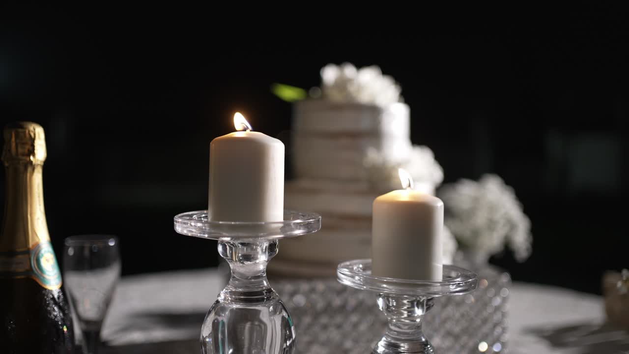 lit white candles beside wedding cake and champagne on a night time reception table