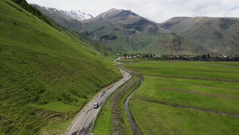 Wide-drone-shot-of-a-road-following-a-vehicle-in-the-Caucasus-mountains-with-Juta-Georgia-in-the-distance