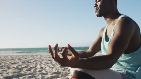 Focused-african-american-man-practicing-yoga-on-beach,-exercising-outdoors-by-the-sea