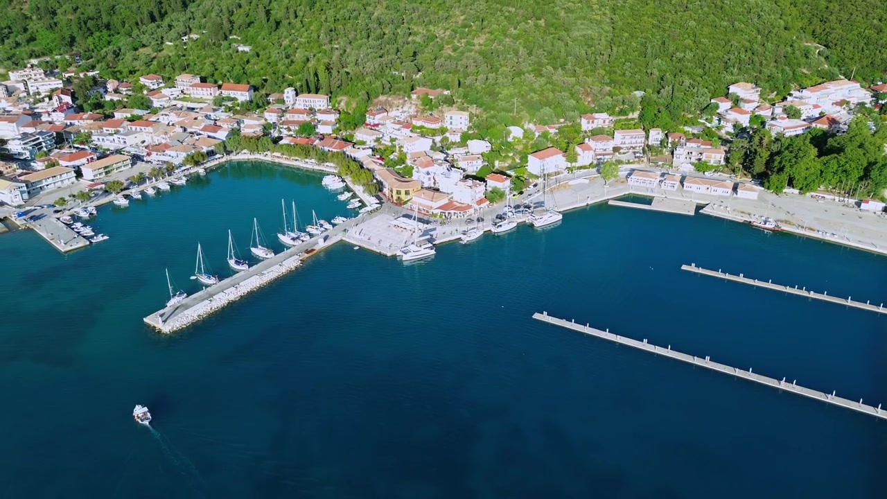 Tomada cinematográfica de drone afastando-se, revelando a pitoresca orla marítima, barcos atracados e casas com telhados vermelhos da vila de Vasiliki em Lefkada, Grécia. Imagens de viagem 4K de alta qualidade.