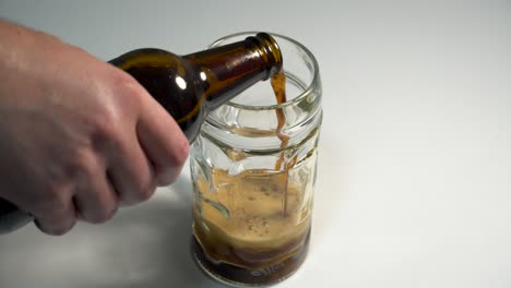 pouring a dark beer with a thick layer of foam into a pint glass on a white tabletop