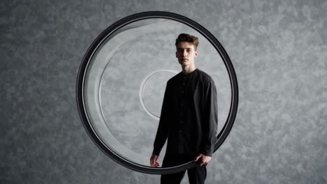 young man posing with a large circular frame on grey background