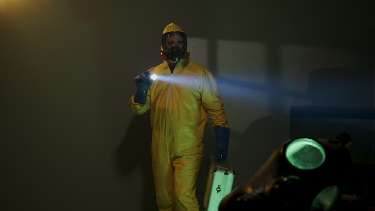 Hazmat suit wearing man explores a dark room