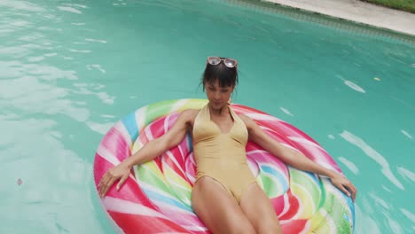 Happy-caucasian-woman-wearing-swimming-suit-with-inflatable-at-swimming-pool-in-garden