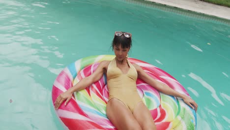 mujer caucásica feliz usando traje de baño con inflable en la piscina en el jardín