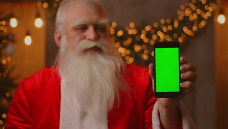 Santa-Señala-Con-El-Dedo-La-Pantalla-Verde-Del-Teléfono-Móvil.-Venta-De-Navidad.-El-Anciano-Papá-Noel-Muestra-Una-Pantalla-Con-Un-Cromakey.-Imágenes-4k-De-Alta-Calidad