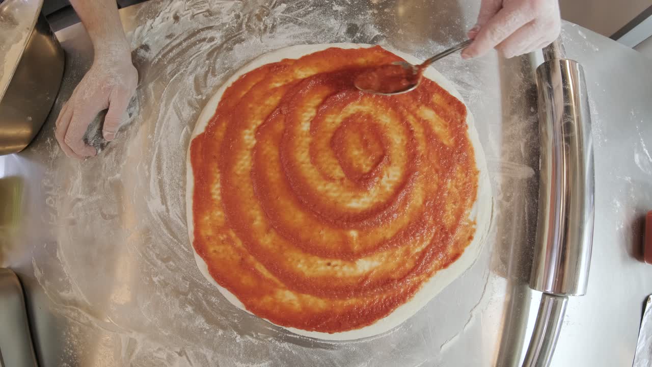 шеф-повар распространяет томатный соус на пиццевое тесто с металлической ложкой в пиццерийном ресторане