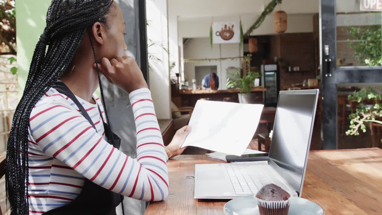 African american female coffee shop owner using laptop and doing paperwork outside, slow motion