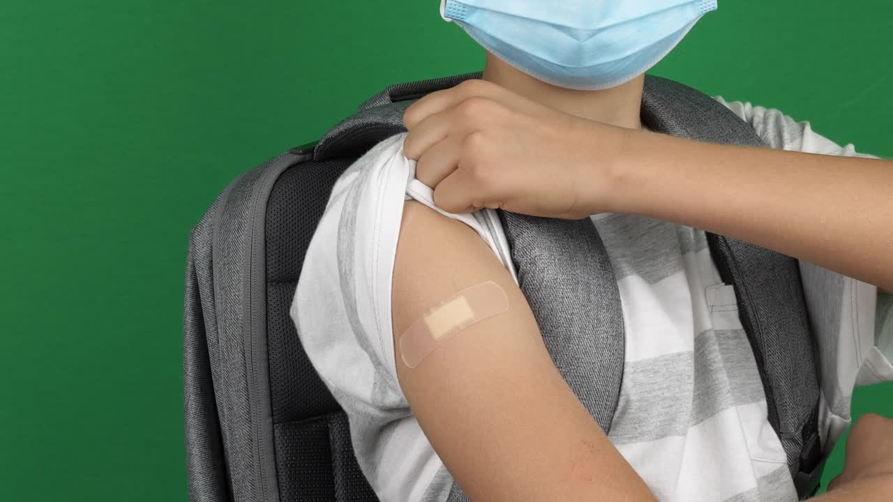 Adolescente com máscara protetora médica apontando para o braço com curativo após vacinação sobre fundo de tela verde. Conceito de vacina, saúde, volta às aulas, viagem