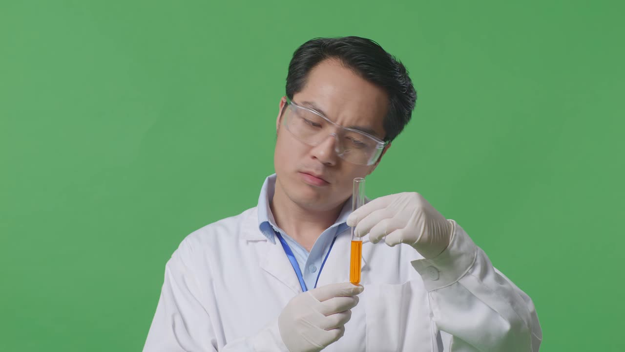 실험실에서 녹색 스크린 배경에 서 있는 동안 두통을 가진 실험 튜브에 오렌지 액체와 함께 아시아 남자 과학자의 근접