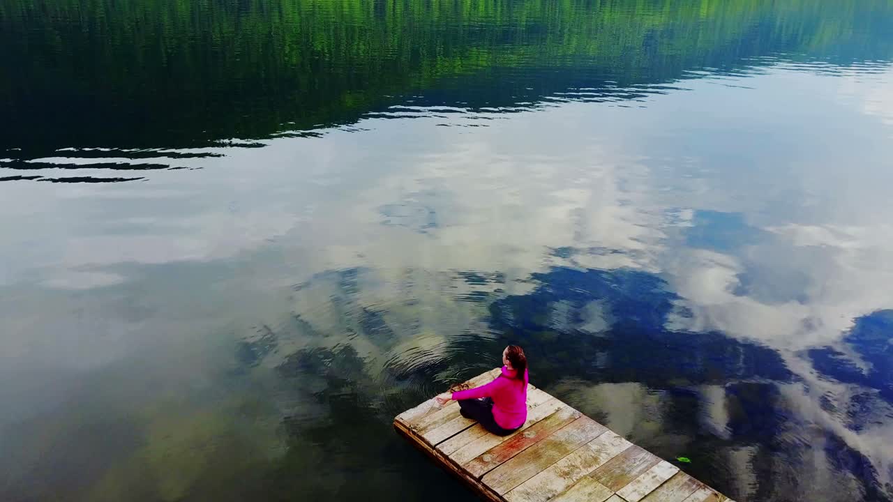 Woman Meditating on a Wooden Dock by a Calm Lake
