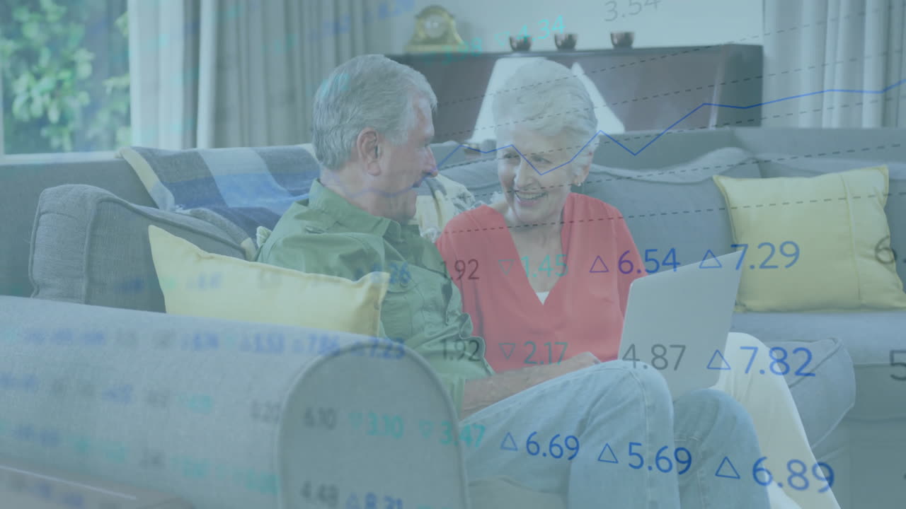 Senior couple reviewing investment data on laptop in living room, showing animated financial graphs