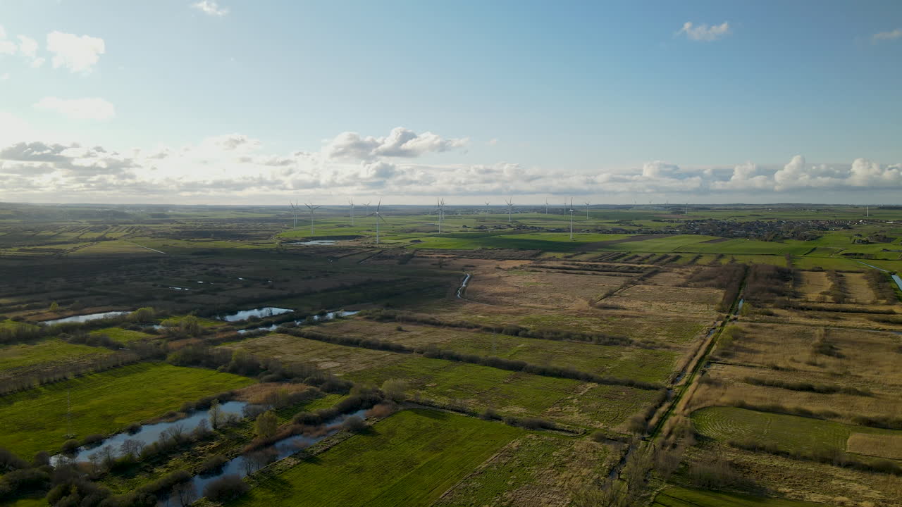 Aerial drone shot of farm fields with rotating wind turbines and lakes near of small polish village in summer