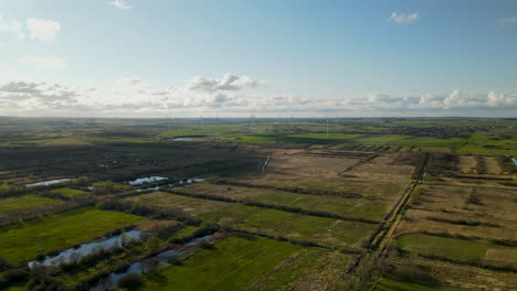 aerial drone shot of farm fields with rotating wind turbines and lakes near of small polish village in summer