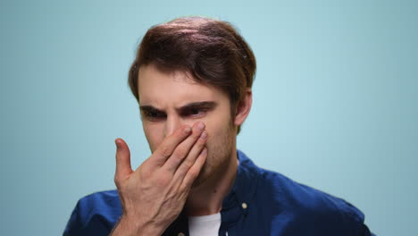 handsome man checking freshness of breath. guy smelling air from mouth in studio