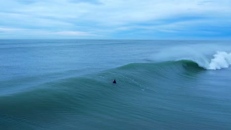 Unrecognizable-surfer-swimming-in-ocean-with-big-waves-crashing