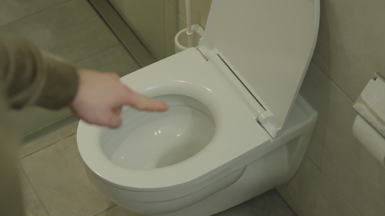 Close-up of a hand pointing at the inside of a toilet bowl, showing where to clean, symbolizing bathroom hygiene, cleaning instructions, and sanitation