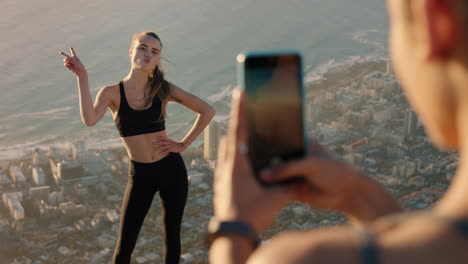 women friends taking photo on mountain top using smartphone camera beautiful influencer woman posing for friend with mobile phone sharing hiking adventure on social media