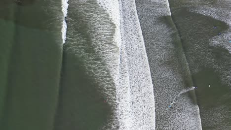 Top-down-shot-overhead-a-small-group-of-surfers-trying-to-catch-a-wave